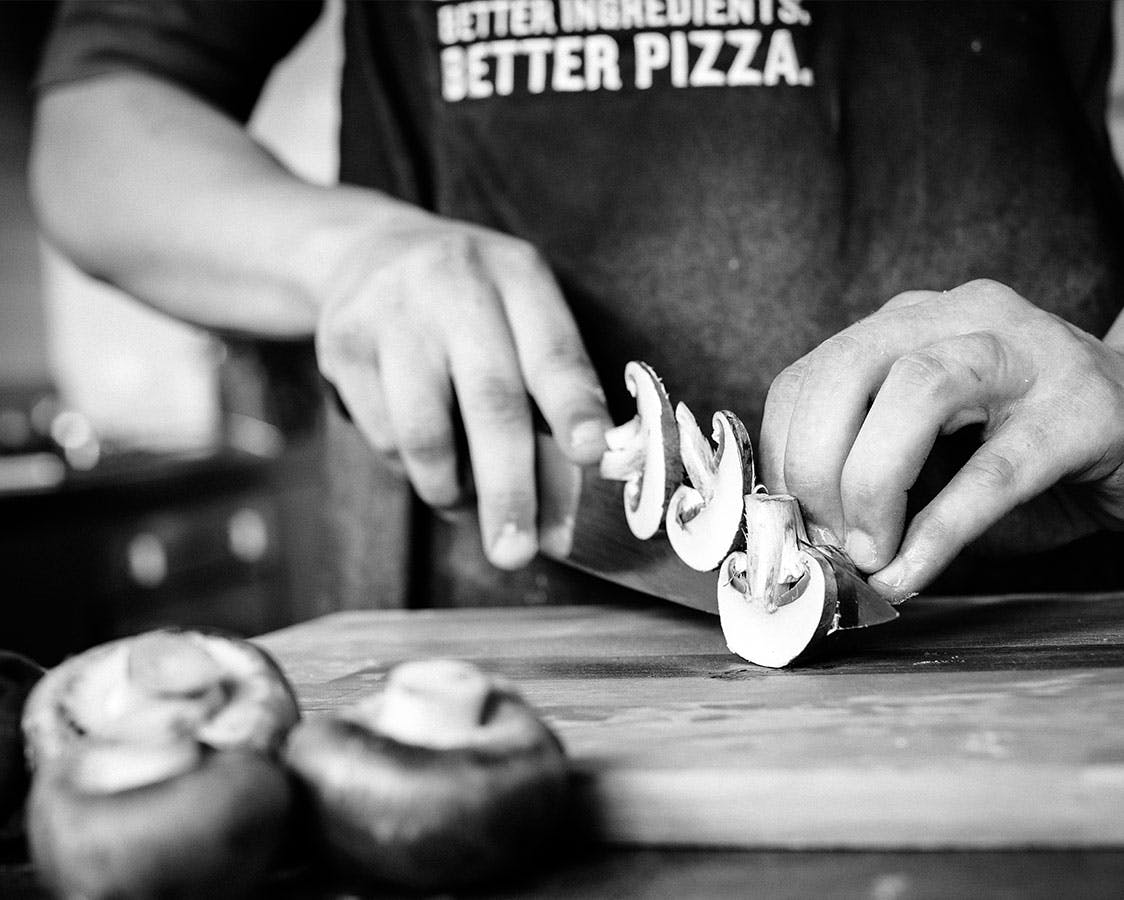 A pizza chef chopping mushrooms wearing a Papa John's apron